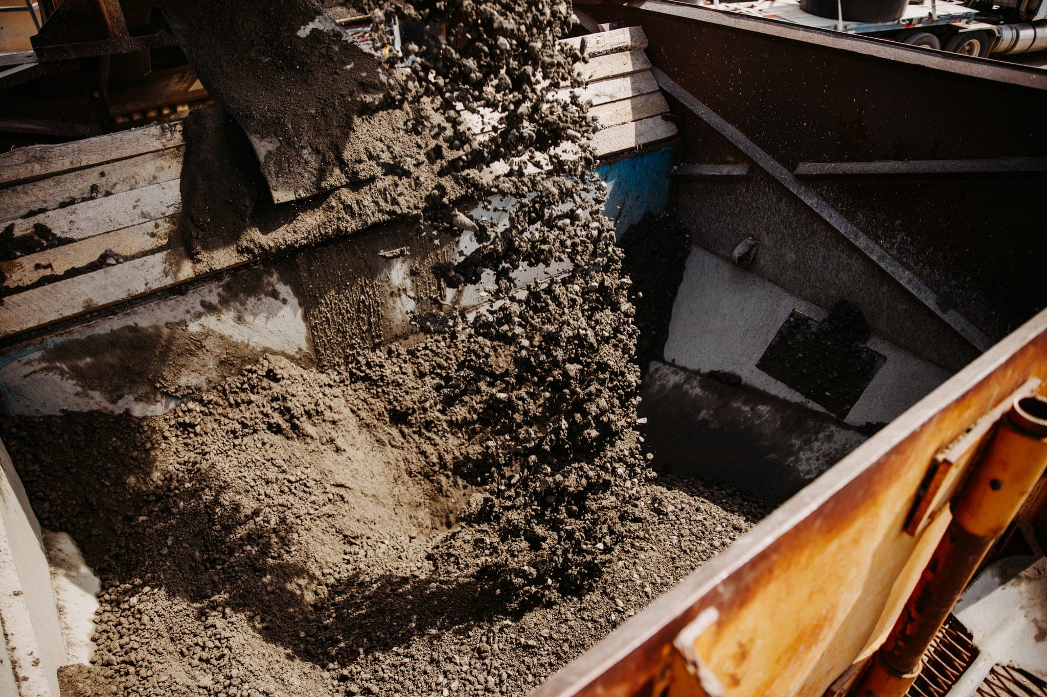 Overhead detail looking into a wood-sided bin as dark roller-compacted concrete material is dumped inside.